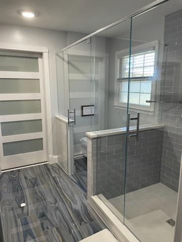 This shower door and toilet partition combination is becoming more popular! This style features two swinging doors with a header system and a half panel on the half wall.